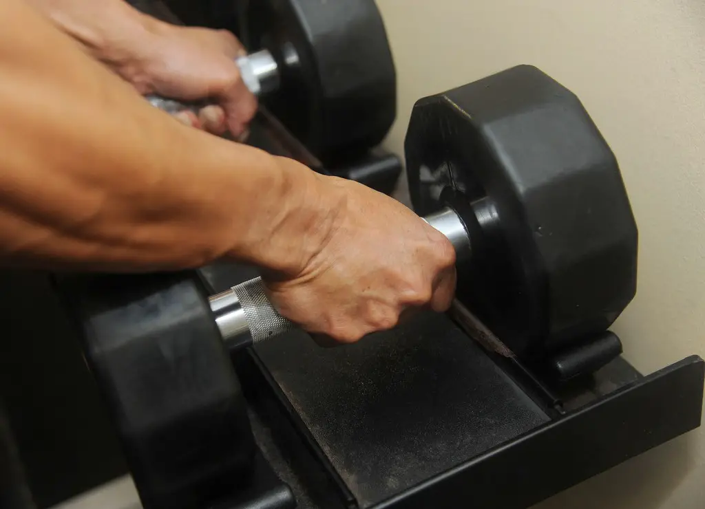list_of_dumbell_exercises_003 man picking up two heavy dumbbells from rack