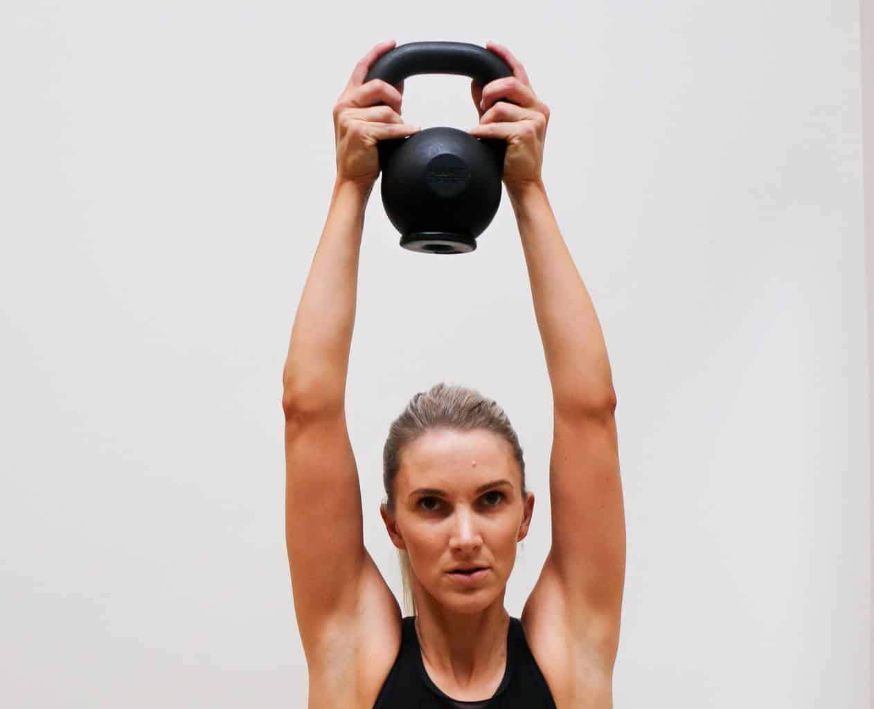 best_shoulder_stability_exercises_004 Woman in sports attire carrying a black kettlebell over her head