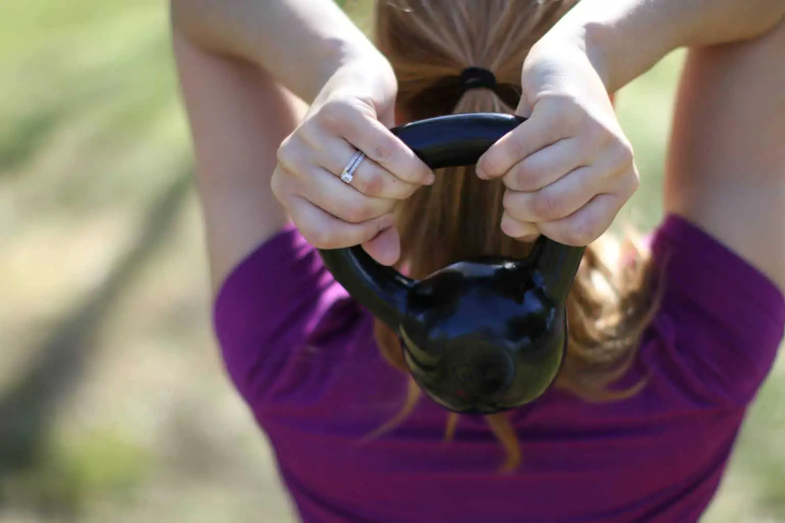 Woman lifting a kettlebell with both hands over her upper back