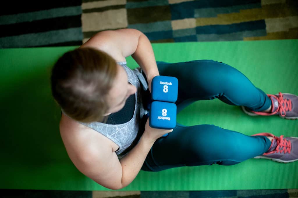 Woman sitting on a green yoga mat with 8 pound dumbbells