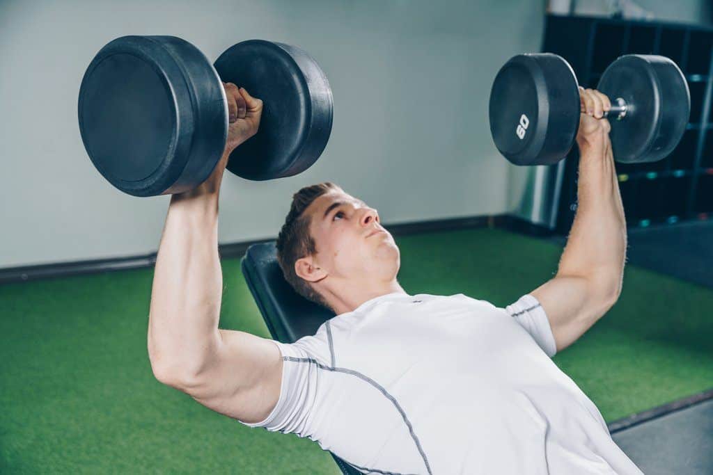 man doing a bench press with two dumbbells