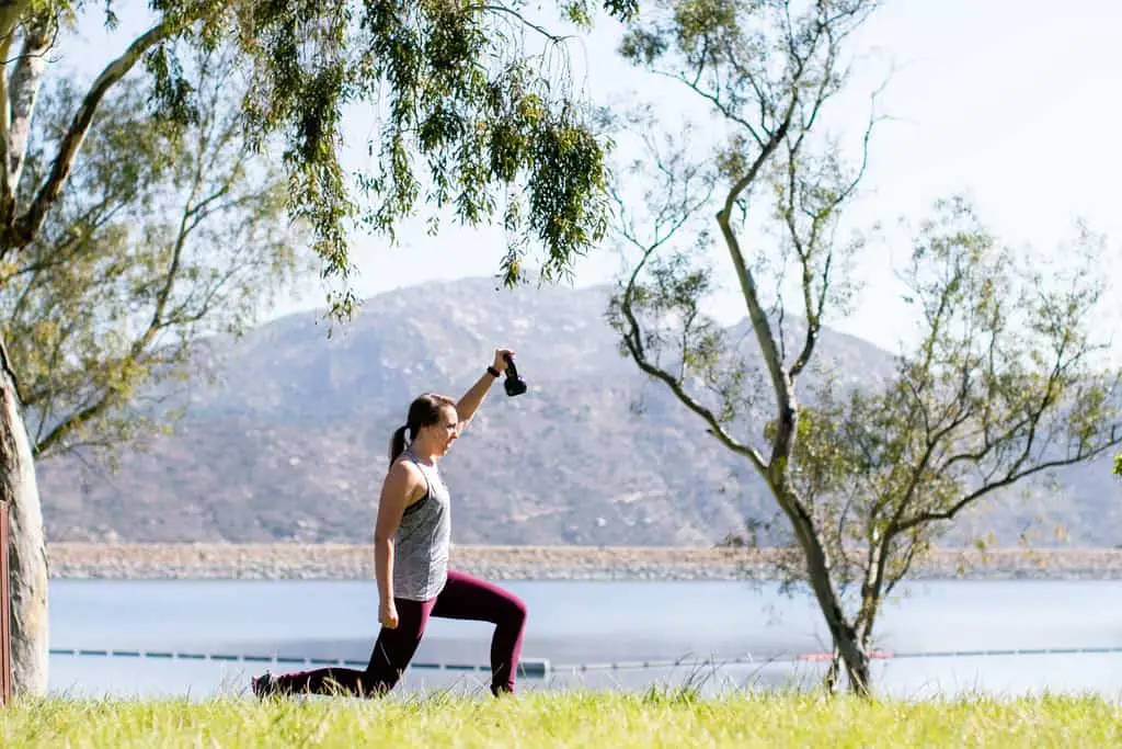 Women performing kettlebell lunges in a park overlooking a lake