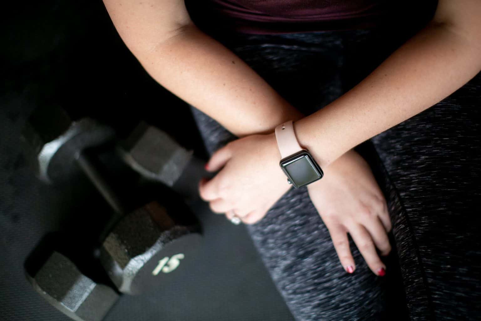 Person sitting down wearing a fitness watch while two dumbbells are in the floor