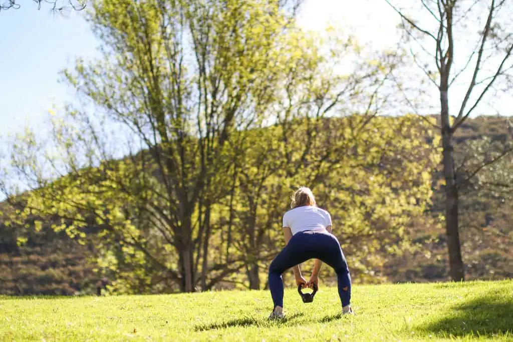Women does kettlebell goblet squat in an open grass field