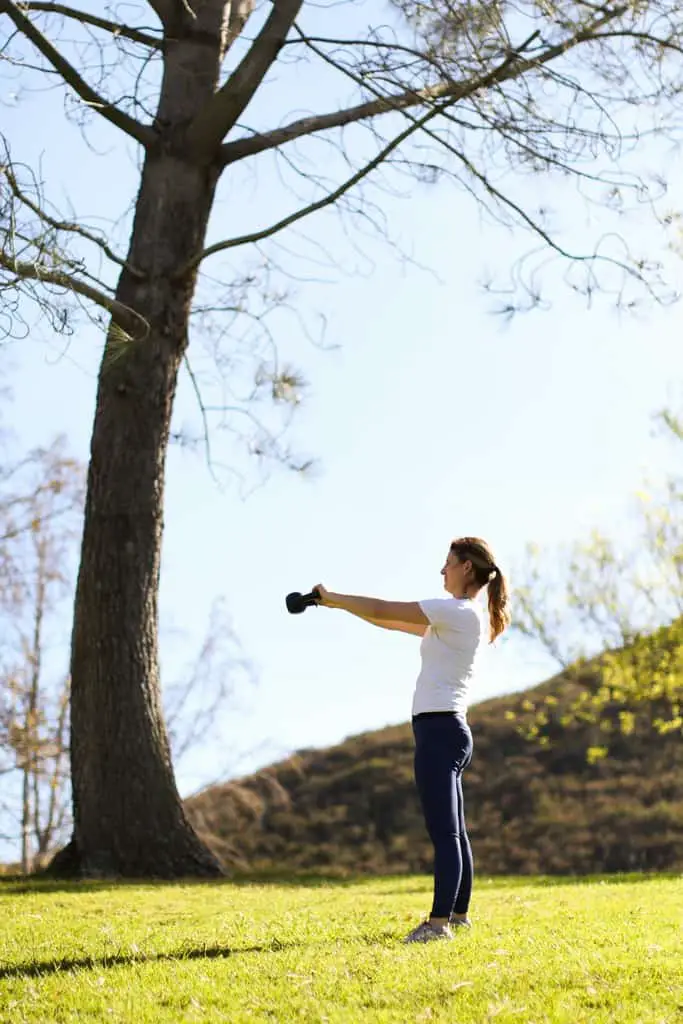Woman does a single kettlebell workout on a green hillside outdoors