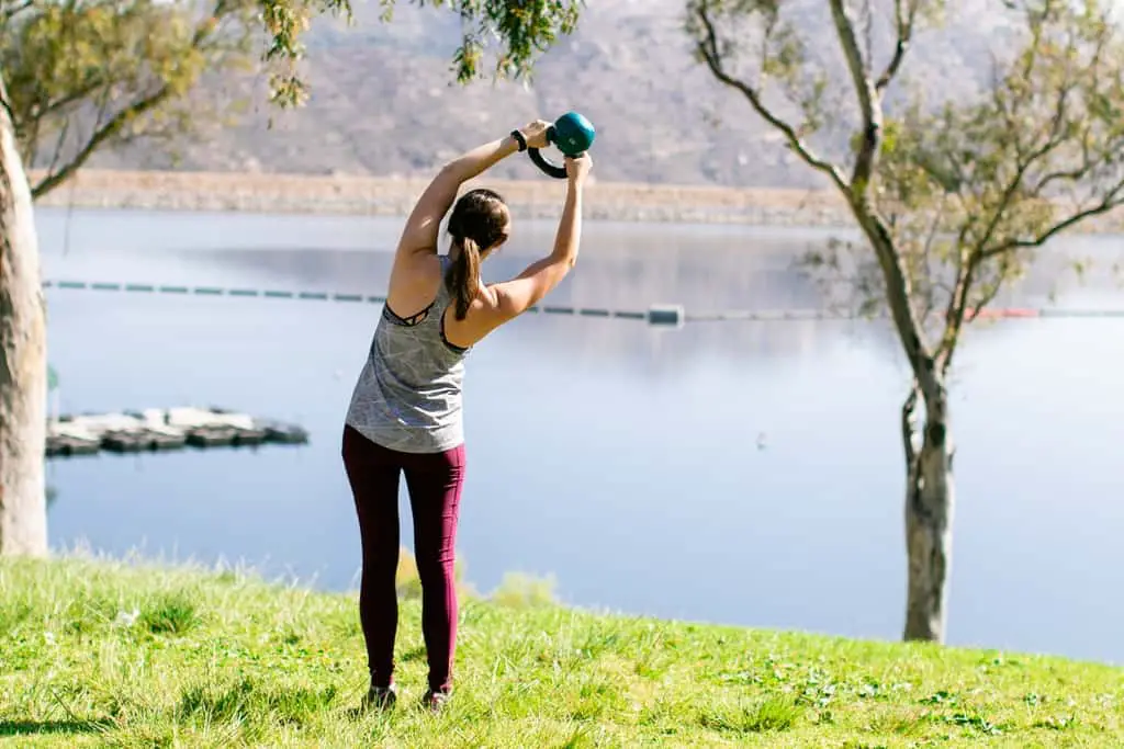 Young women does a beginner kettlebell workout by a scenic lake