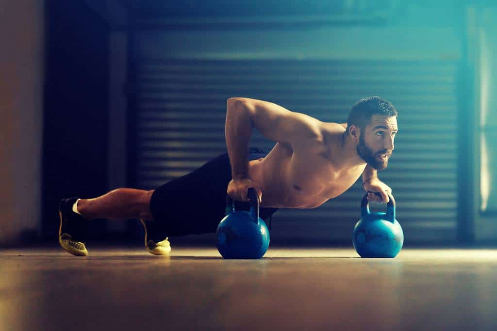 kettlebell-cardio-training-1 A man does kettlebell cardio training by doing pushups with 2 bells