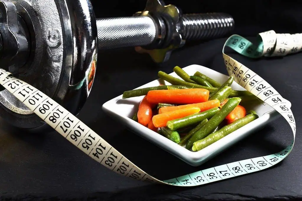A dumbbell, a tape measure, and a plate full of vegetables
