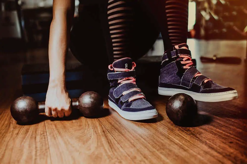 A woman about to pick up one piece of a dumbbell while one foot is resting on the other set