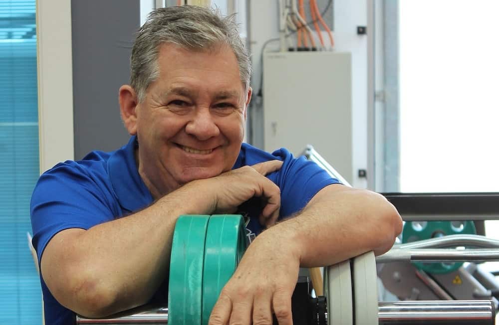 Older man sitting down while touching an adjustable dumbbell