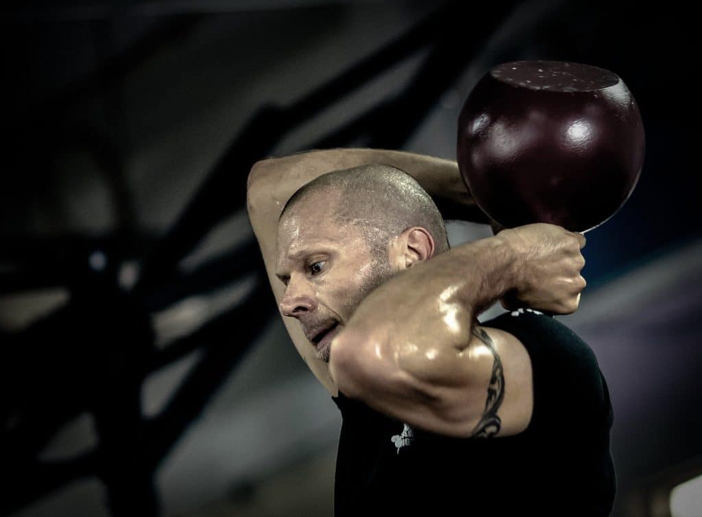 Man swinging a kettlebell over his head with both of his hands