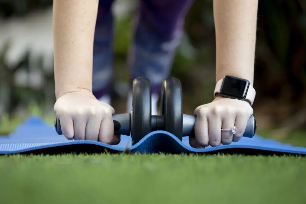 Person using an ab roller with a blue yoga mat in their lawn