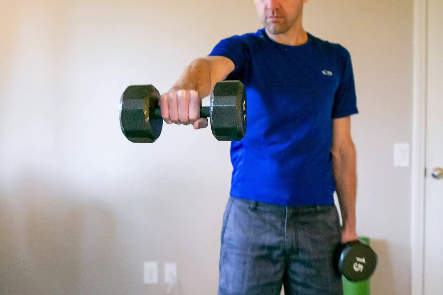 Man lifting a dumbbell across his chest while holding the other one near his sides