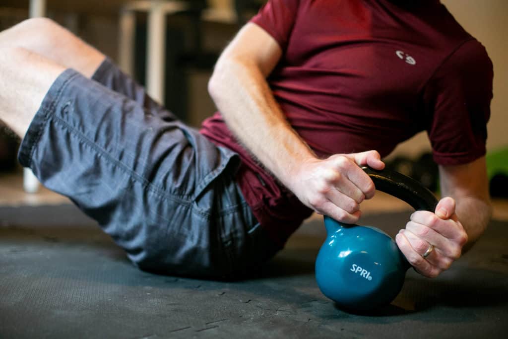 Man doing a Russian twist with a kettlebell on his gym flooring at home