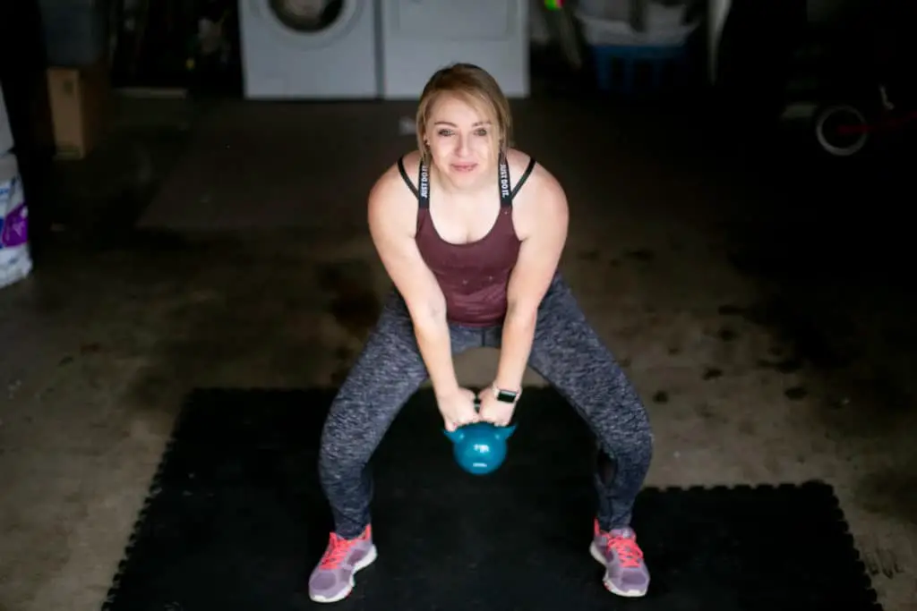 Woman doing a kettlebell swing in her garage that doubles as a workout space
