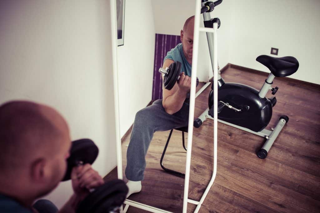 Man lifting a dumbbell with one hand while sitting down and looking back at a mirror