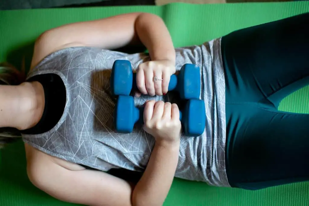 Woman lying flat on her back while holding two dumbbells with each hand on her stomach