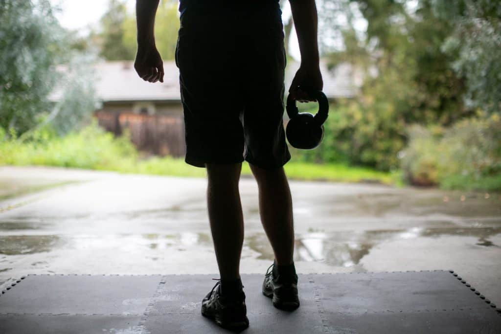 Silhouette of a person standing in their garage holding a kettlebell with one hand