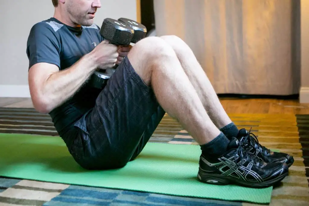 Man sitting down on the floor while holding dumbbells with each hand