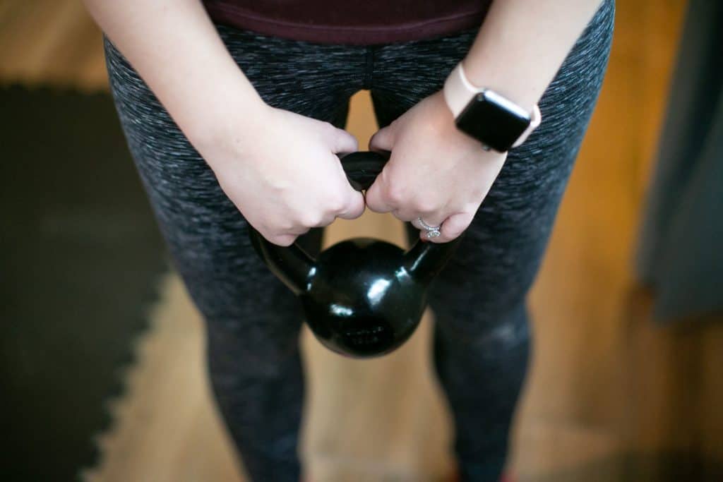 Woman wearing a fitness tracker while holding a kettlebell with both hands