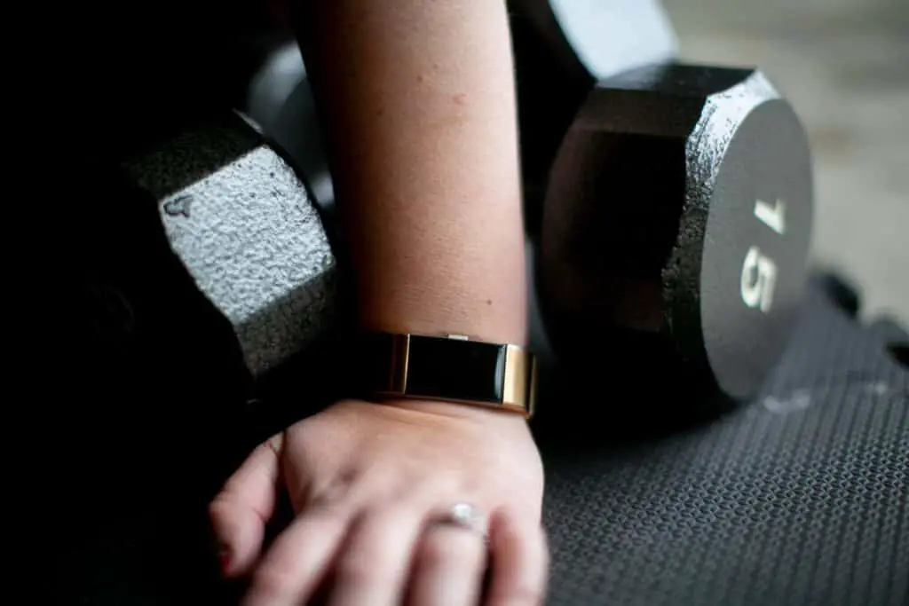 Close up of a person's hand wearing a fitness watch beside a pair 15 kg dumbbells