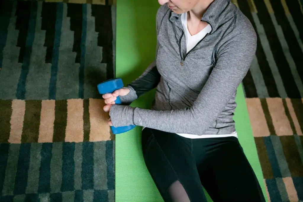Woman sitting down on the floor while trying to lift a dumbbell