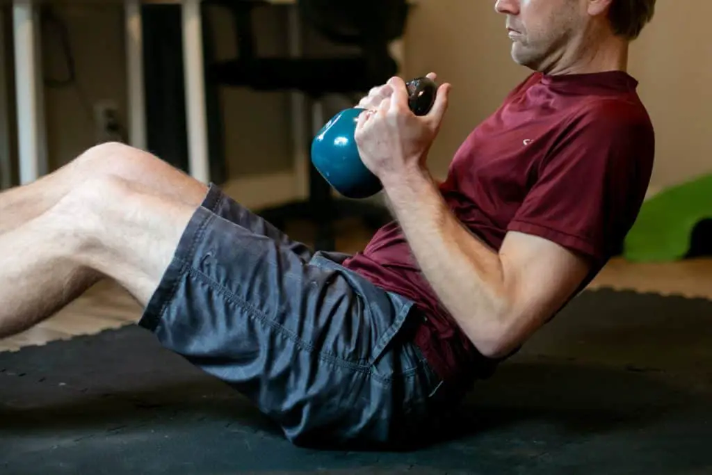 Man doing crunches while holding a kettlebell with both hands