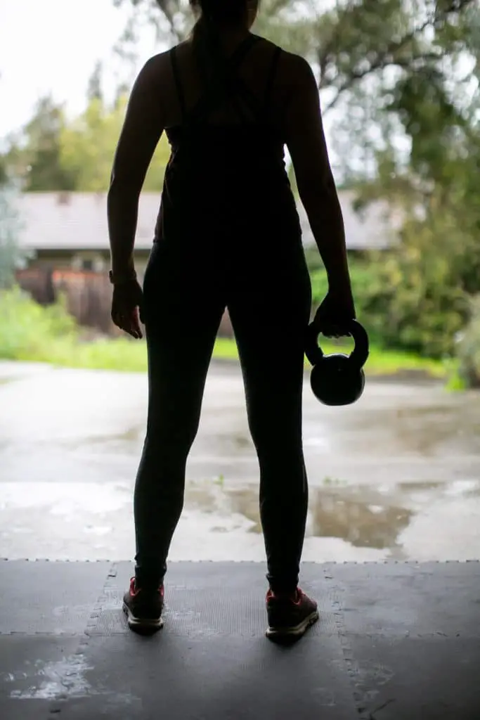 Silhouette of a person standing in their garage holding a kettlebell with one hand
