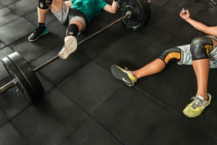Two men lying on the floor wearing knee sleeves while resting from a fitness routine
