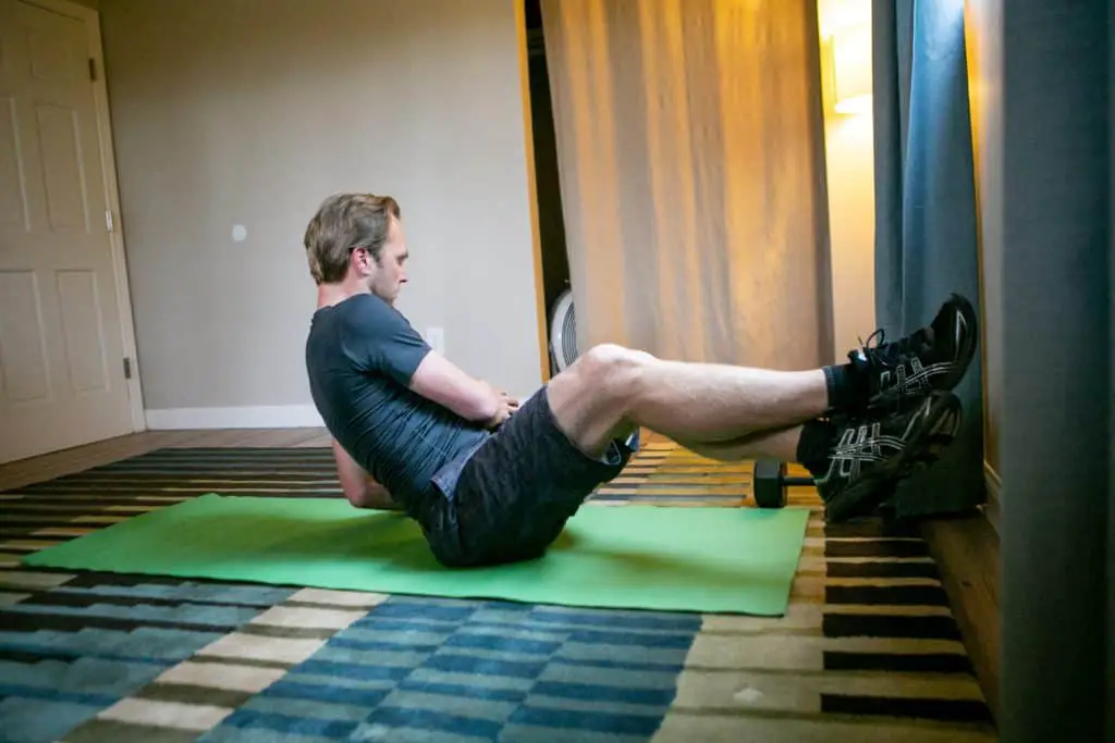 Man sitting on the floor with his legs lifted in the air while holding a dumbbell on his side