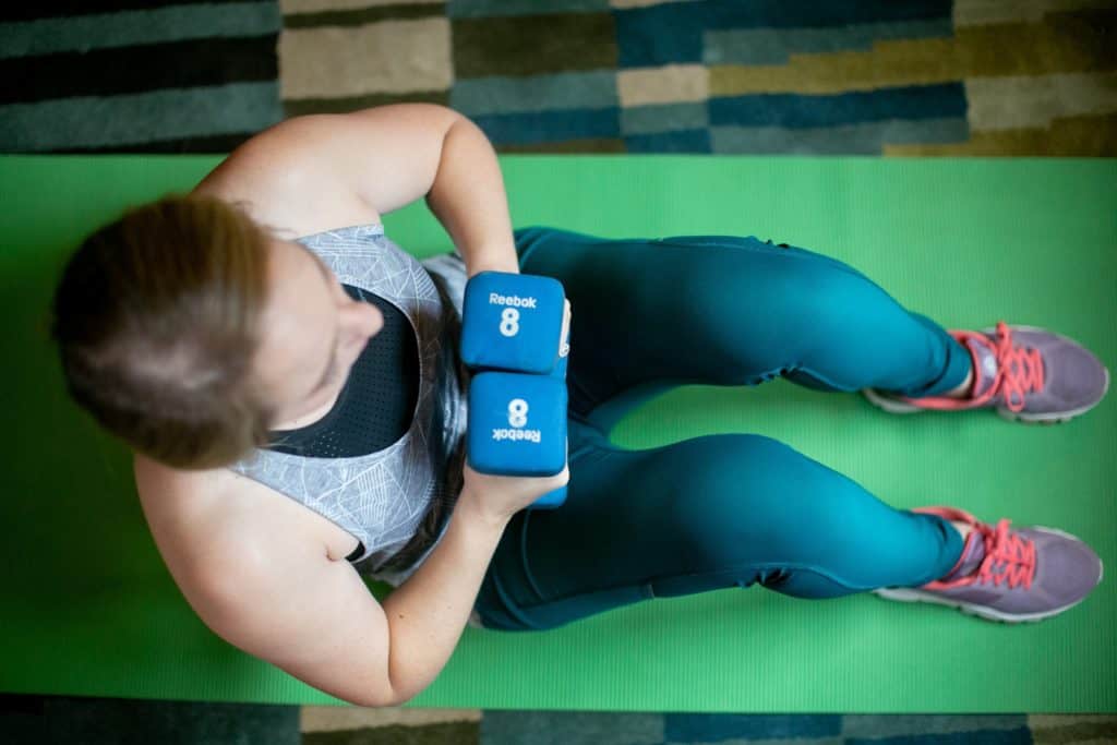 Woman sitting down on the floor while holding dumbbells with each hand