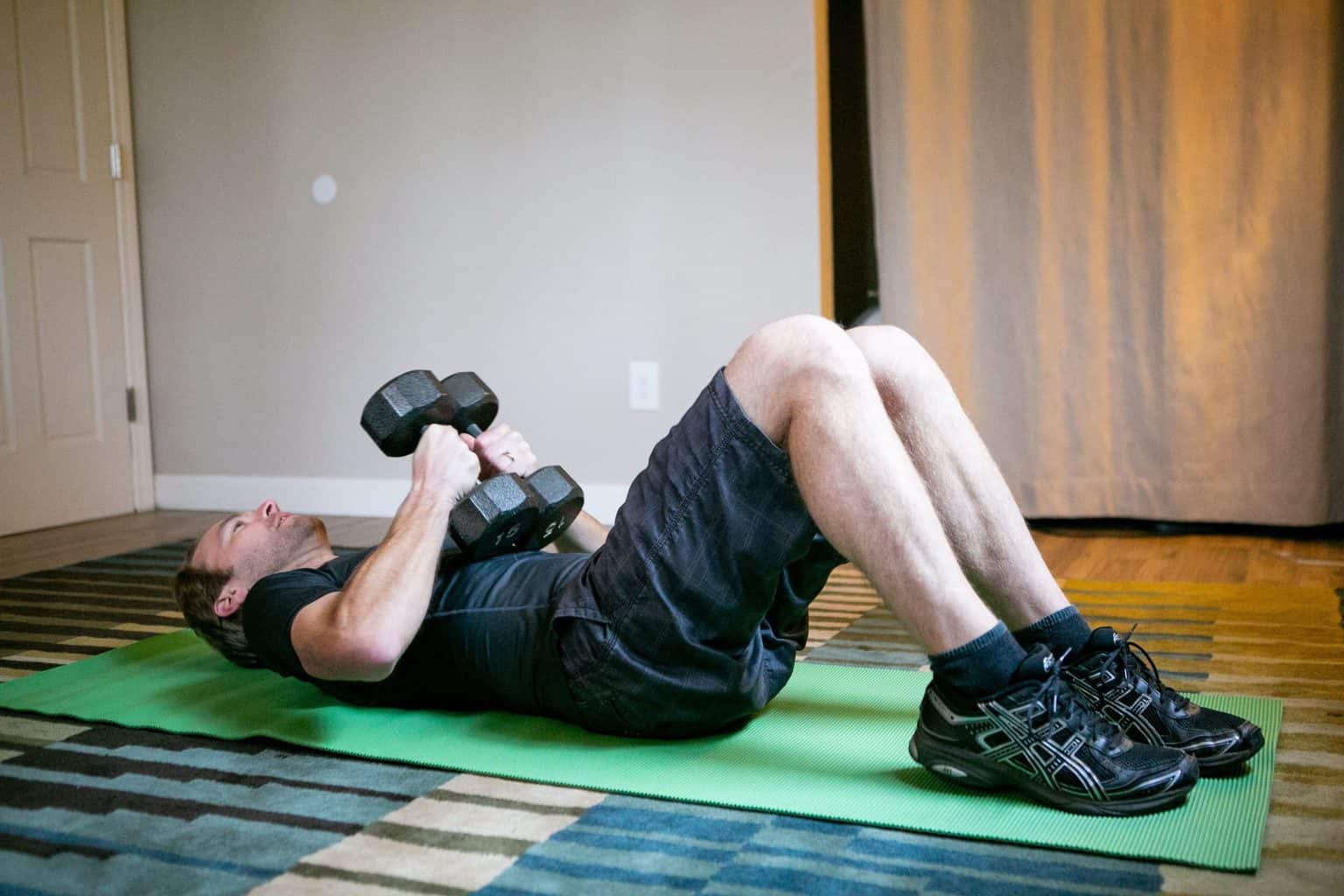 Man lying down on his back while holding a pair of dumbbells