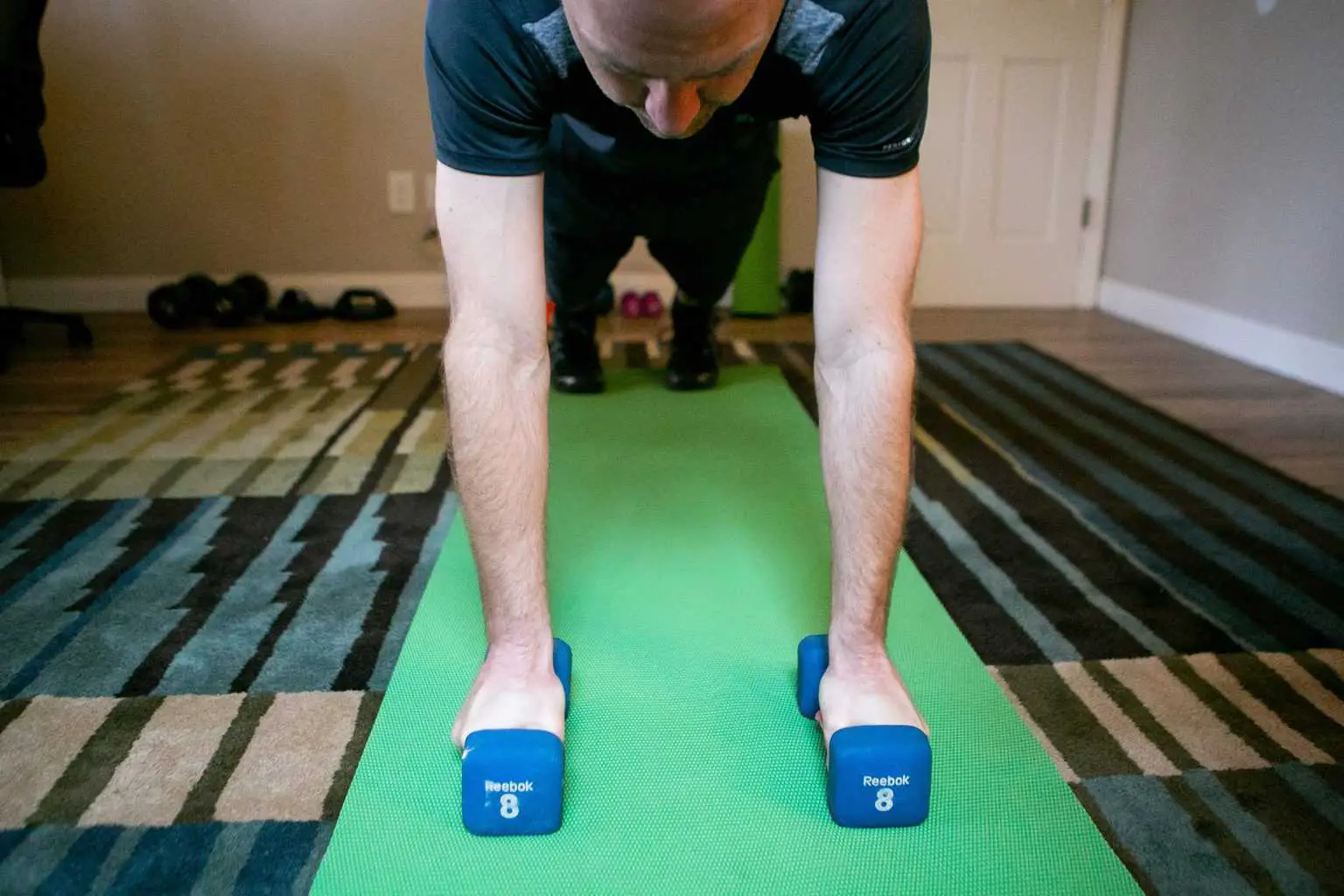 Man in a plank position while holding dumbbells with each hand