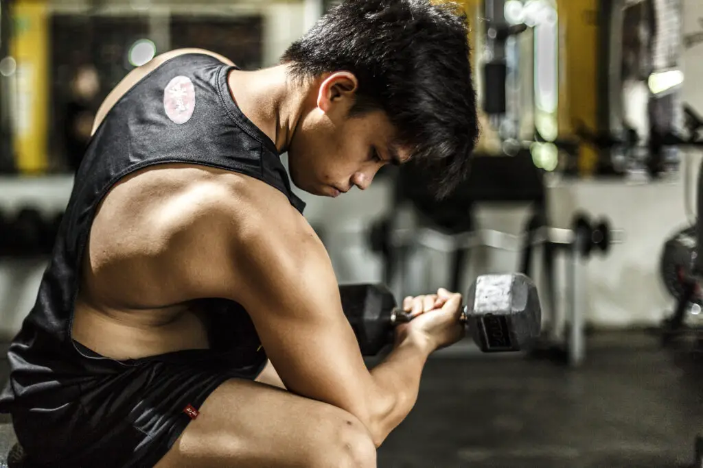 Woman sitting on a bench while trying to lift a dumbbell with one hand