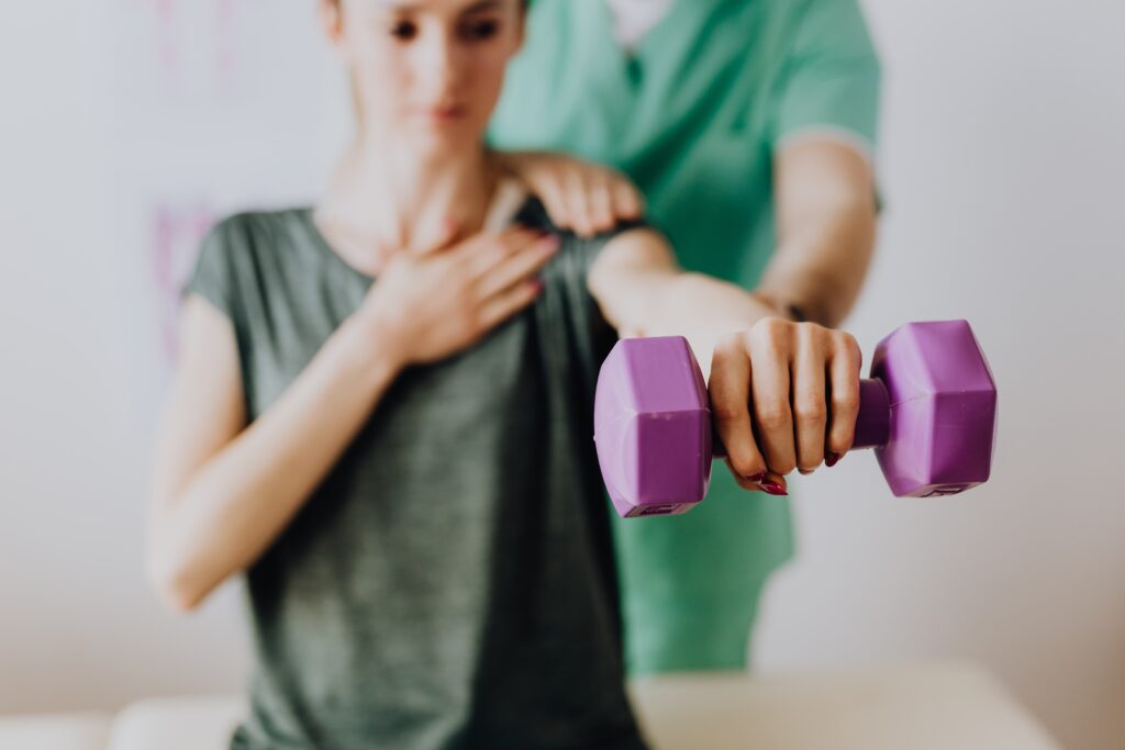 Woman being helped by a trainer while building strength with dumbbells