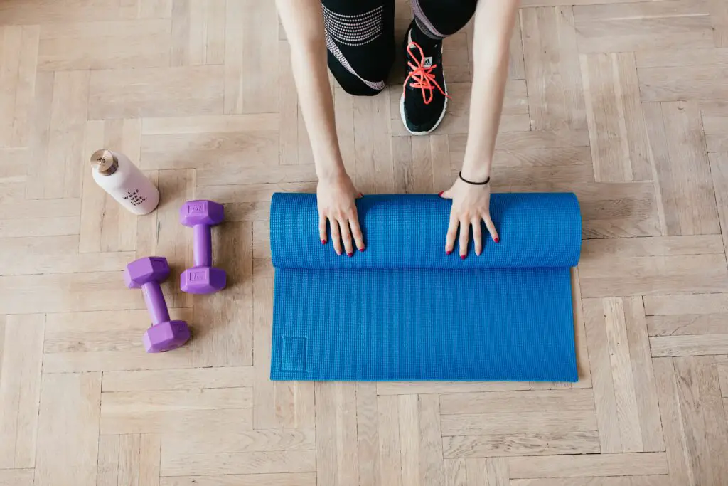 Woman folding her mat with a pair of dumbbells and water bottle beside her