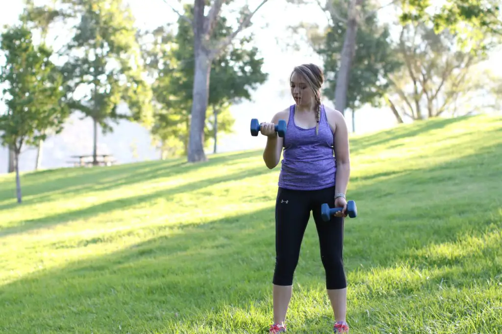 Woman lifting a dumbbell with one arm while holding the other pair on her side