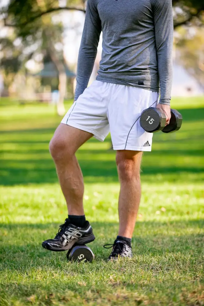 Man holding a dumbbell with one hand while stepping on the other pair on the grass