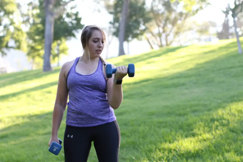 Woman lifting a dumbbell with one arm while holding the other pair on her side