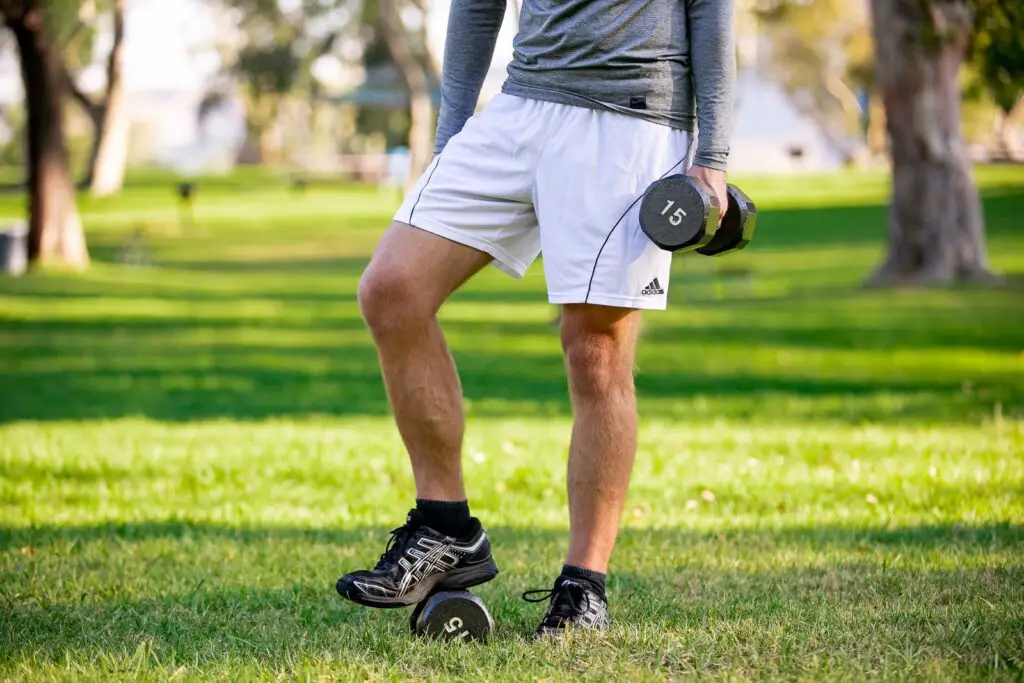 Man holding a dumbbell with one hand while stepping on another one on the grass