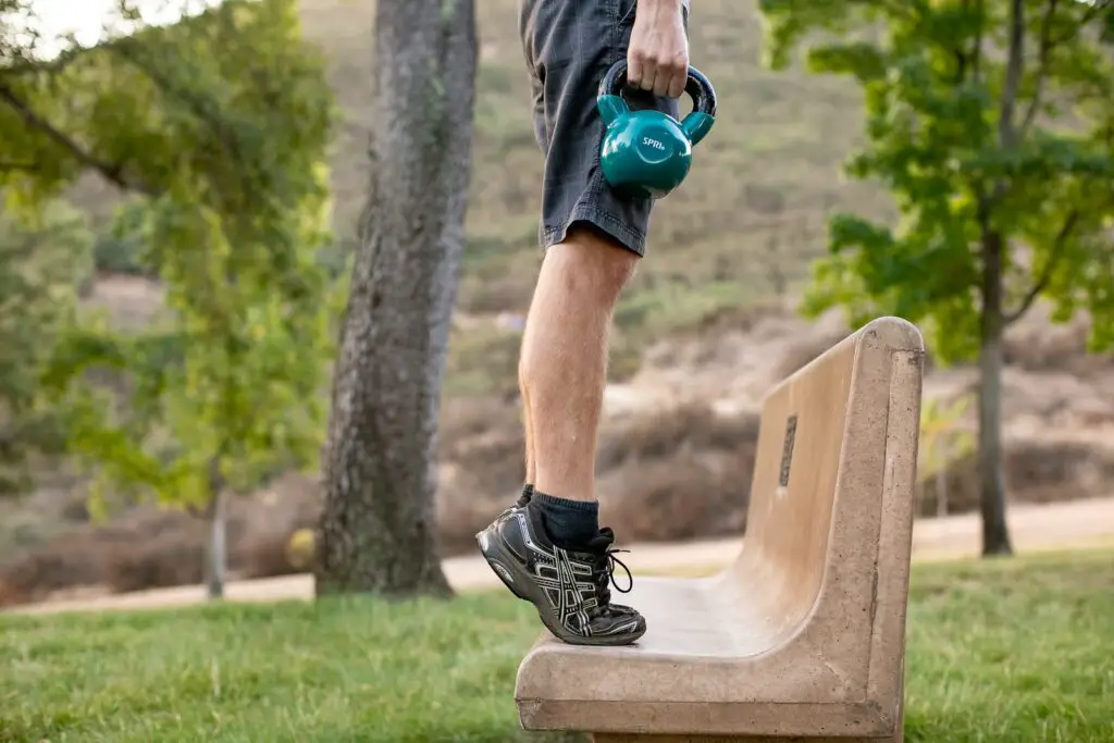 Person holding a kettlebell with one hand while standing tip toed