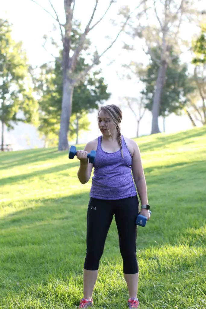 Woman lifting a dumbbell with one arm while holding the other pair on her side