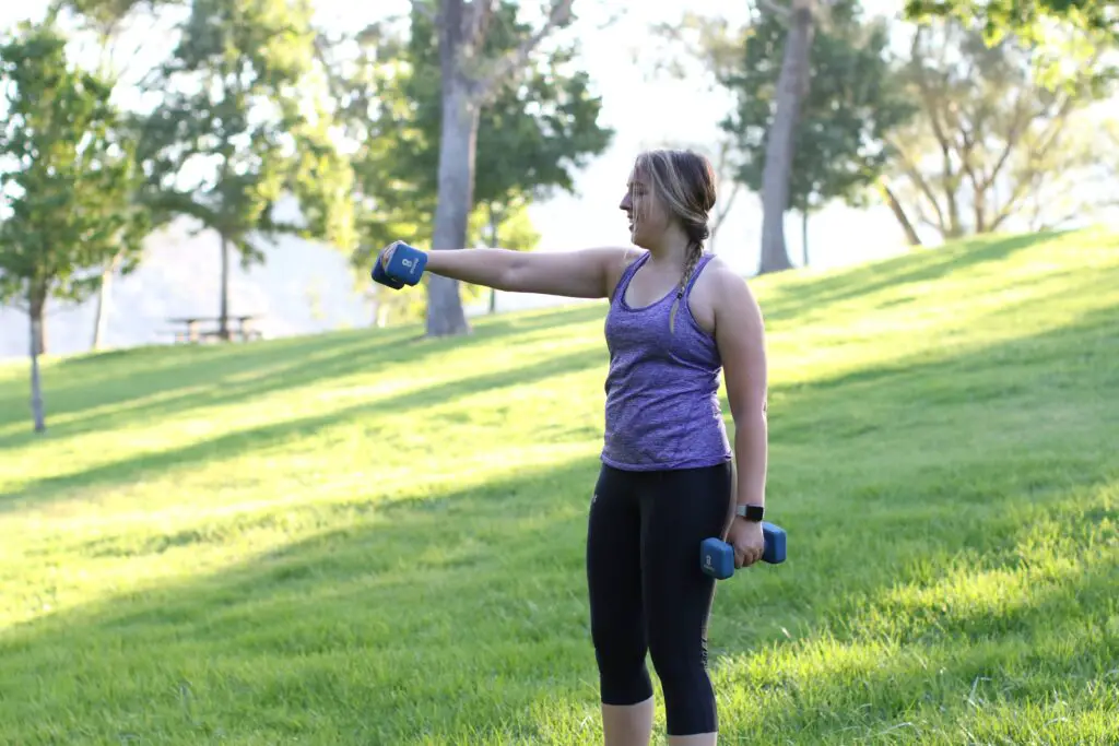 Woman lifting a dumbbell on her chest level, while holding the other pair on her side