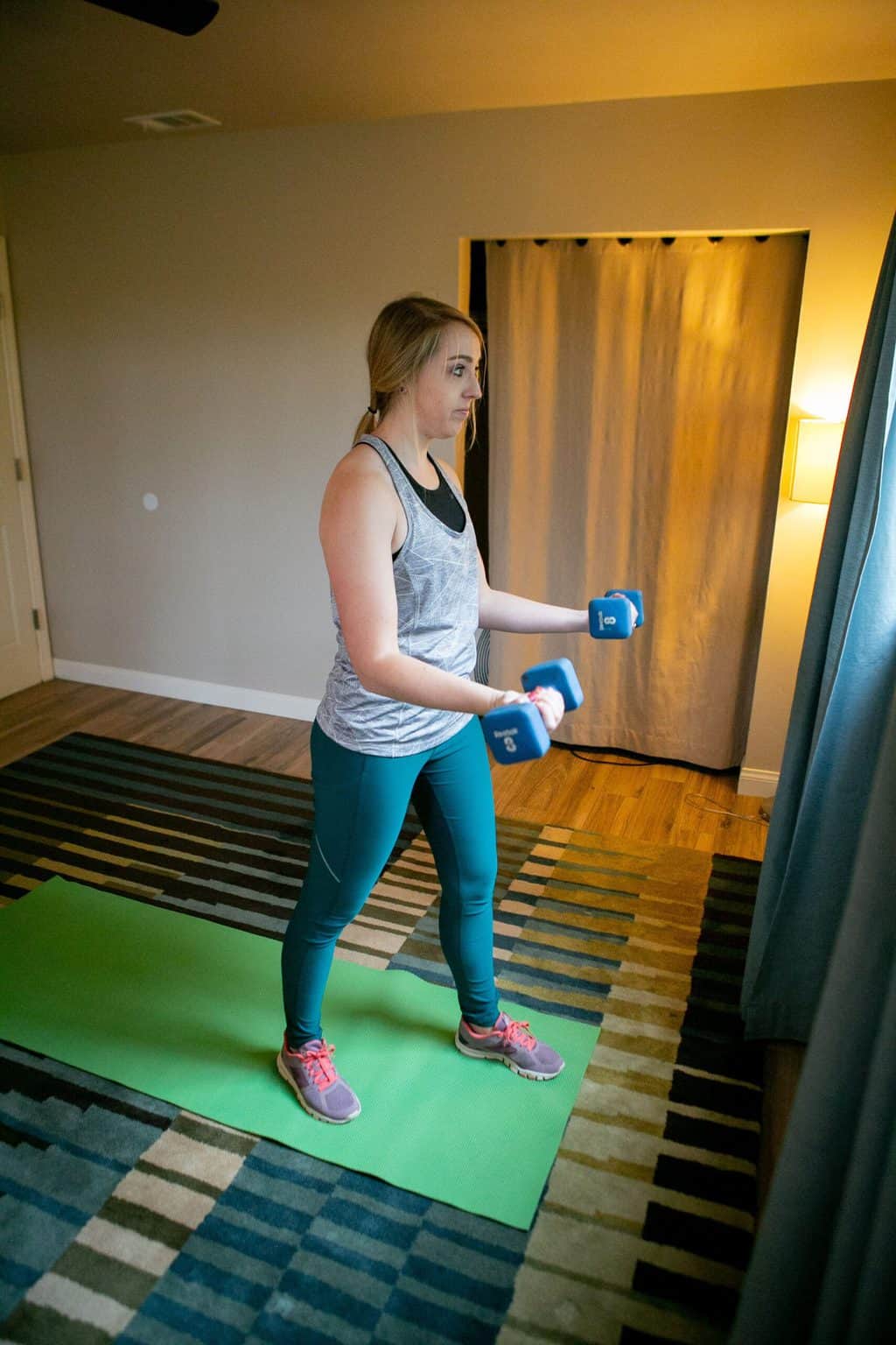 Woman standing on a green mat while lifting dumbbells