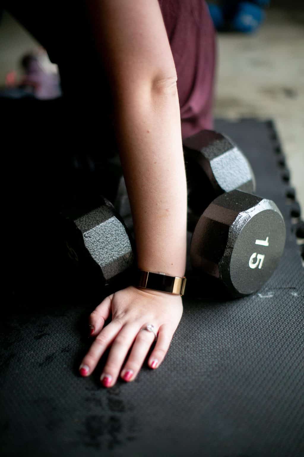 Close up of a person's hand wearing a fitness watch beside a pair 15 kg dumbbells