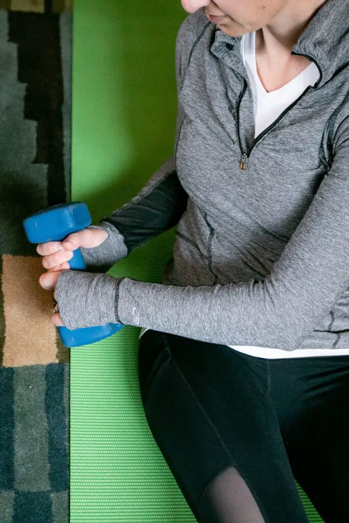 Woman sitting down trying to lift a dumbbell with both hands